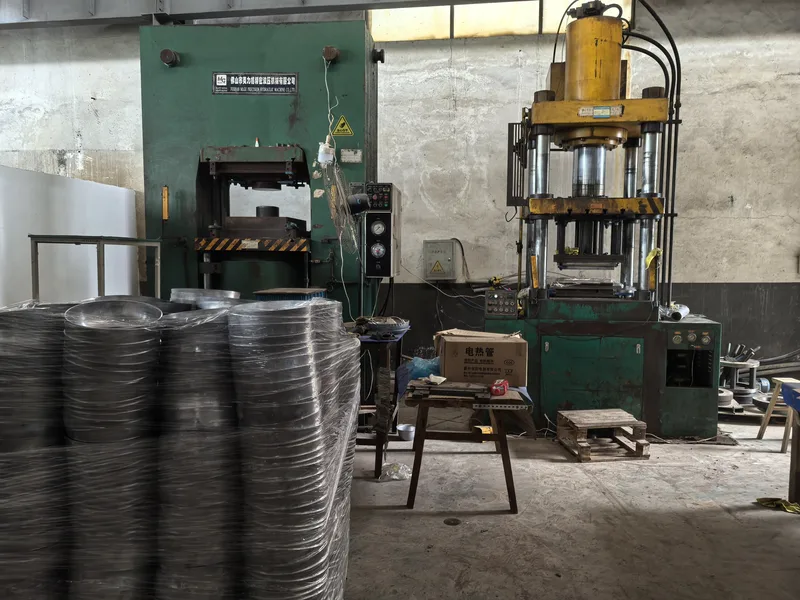 Metalworking presses beside stacked cookware bodies