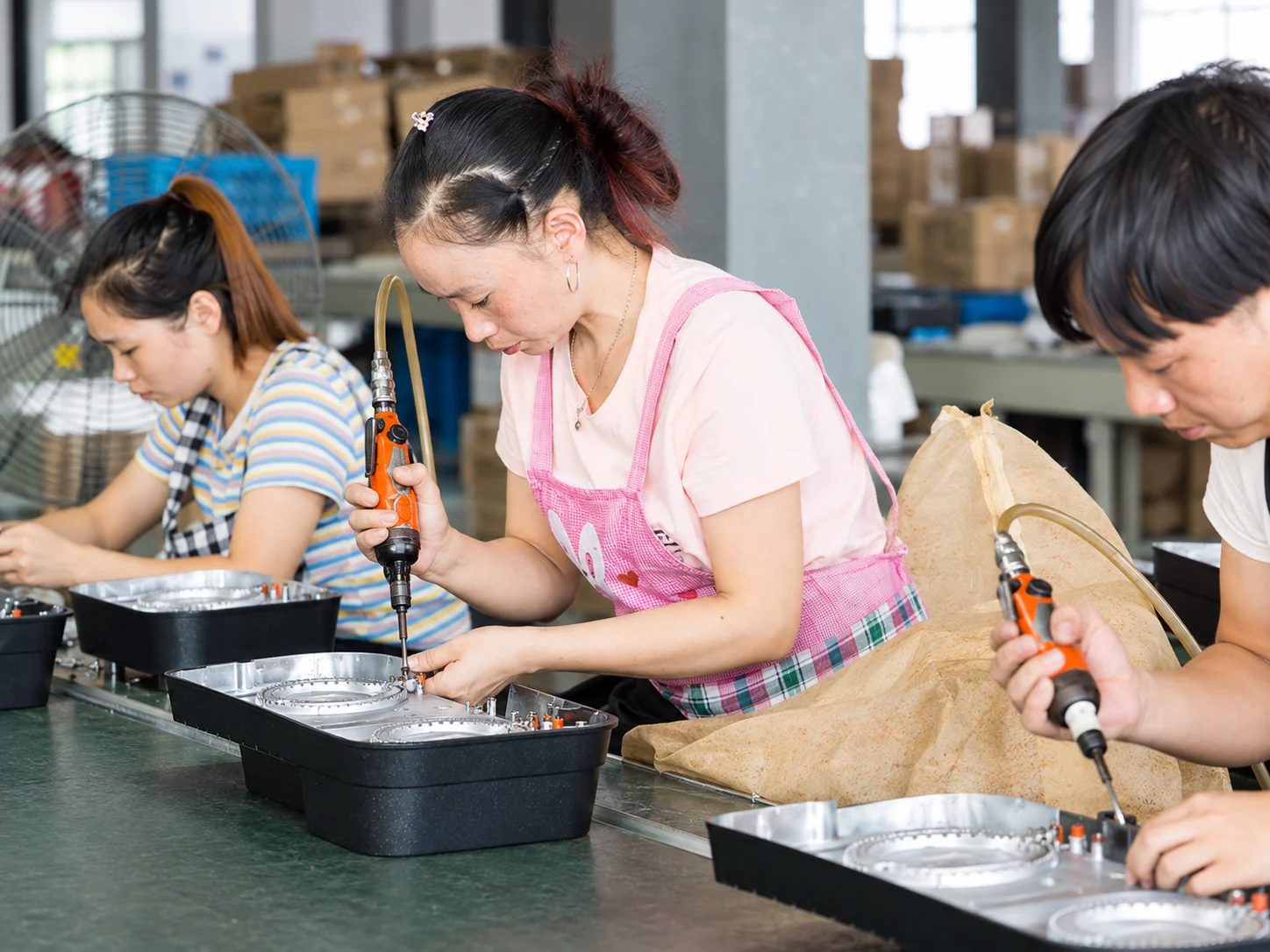 Staff assembling cookware components with handheld tools.